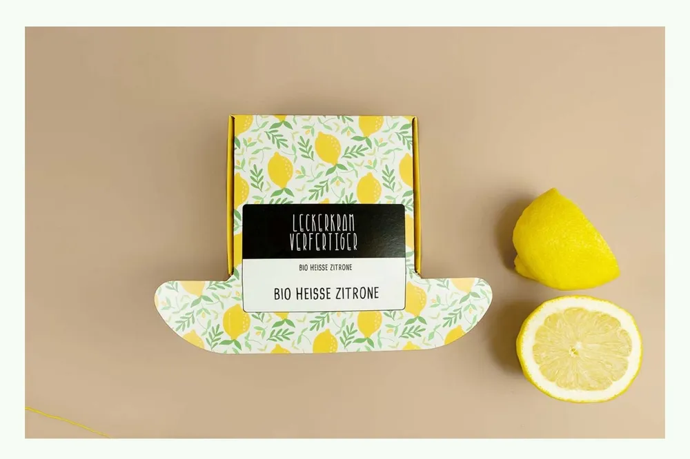 Bedruckte Klappschachtel mit Zitronendesign neben frischen Zitronen Bedruckte Klappschachtel mit Zitronendesign neben frischen Zitronen
