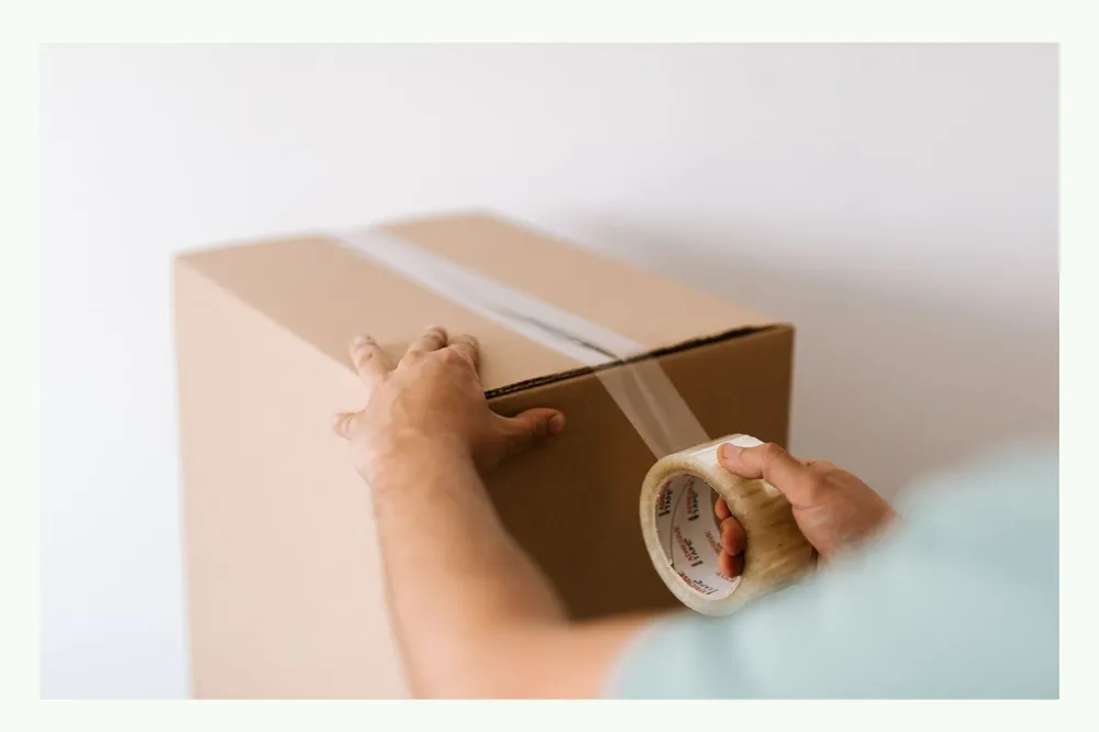 Person sealing a cardboard box with brown packing tape Person sealing a cardboard box with brown packing tape