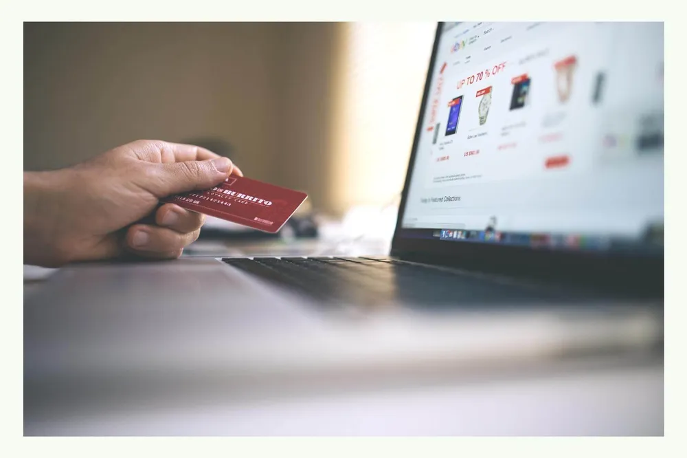 Hand holding a credit card in front of a laptop with an online shop page Hand holding a credit card in front of a laptop with an online shop page