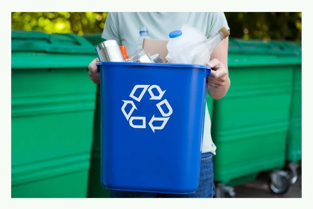 Person holding a blue recycling bin with symbol
