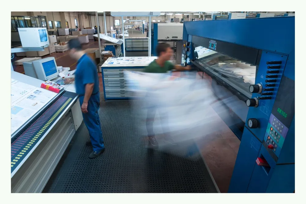 Mitarbeiter arbeiten an einer großen Druckmaschine in einer Produktionshalle